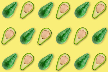 Rows of fresh wholes and halves of organic avocado with kernels on yellow table in kitchen or market. Top view. Cooking concept. Seamless pattern