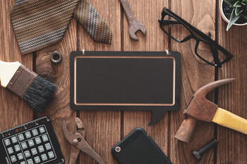 Labor Day and father's day background concept. Flat lay of construction blue collar handy tools and white collar's accessories over wooden background with black chalkboard. 
