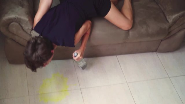 high angle of a boozy woman puking on the floor while laying on the sofa