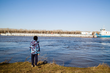 Fototapeta premium The boy on the shore looking at the tug with a barge