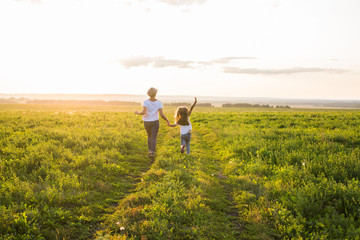 Rear view of mother and daughter running in green field with sunset on background