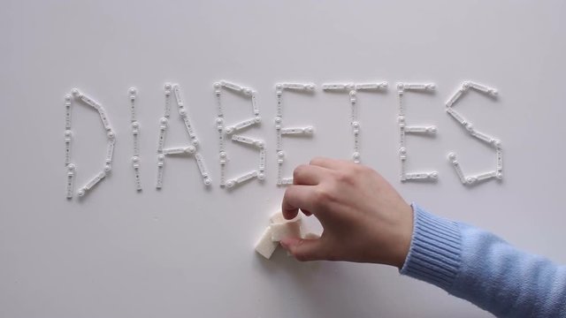 The word DIABETES with lancets for glucometer on the table on a white background. Lay next to the sugar cubes. A woman's hand takes a sugar cube. The concept of type 1 and type 2 diabetes.