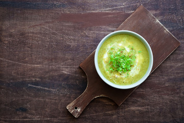 Bowl of broccoli cream soup or zucchini. Brown cutting board and dark plywood background