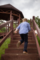 The view from the back of the boy runs along the wooden stairs in the park. Cloudy, the child rushes into the arbor to shelter from the rain. Spring in the park