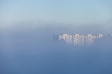 A lonely tall building peeking out from under a dense layer of fog that covered the city in the early morning. City concept. City in the clouds.
