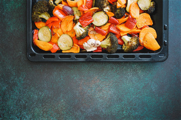 Trays of roasted different vegetables. Zucchini, sweet potatoes, carrots, broccoli, red bell vegetables. Dark green background, copy space