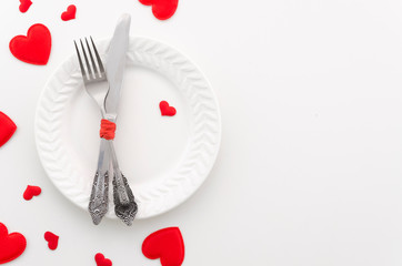 Valentines 14 February romantic dinner concept greeting card fork and knife on white dish. White tablecloth with red hearts and copy space for greeting text. Anniversary copy space text