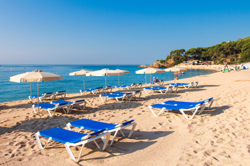 Fototapeta na wymiar Cala de Fenals beach in Lloret de Mar, Costa Brava. Sandy resort beach in Spain with deck chairs and sun umbrella