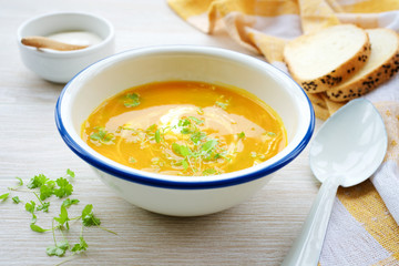 Pumpkin soup in white bowl with cream and parsley. Light wooden background