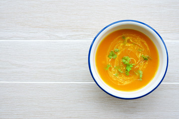 Pumpkin soup in white bowl with cream and parsley. Light wooden background