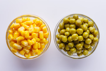 canned corn and green peas in a glass bowl on a white background