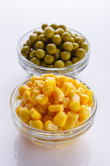 canned corn and green peas in a glass bowl on a white background