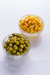 canned corn and green peas in a glass bowl on a white background