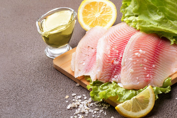 Tilapia fillet with lemon, rosemary and lettuce on a cutting board.