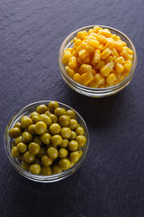 canned corn and green peas in a glass bowl on a dark stone background