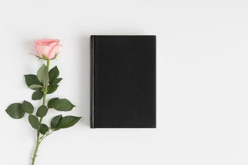 Top view of a black book mockup with a pink rose on a white table.