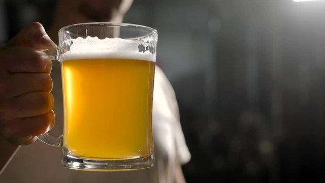 Close-up shot of a brewer raising a glass of a freshly made light beer.