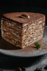 A large piece of chocolate-nut cake sprinkled with cocoa. On a gray plate with a sprig of mint. Close-up. Dark photo.