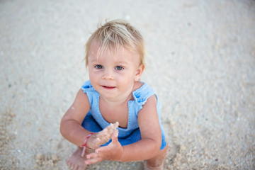 Cute toddler baby boy playing with sand on tropical beach, cute shot from above, baby smiling, wearing knitted onesie