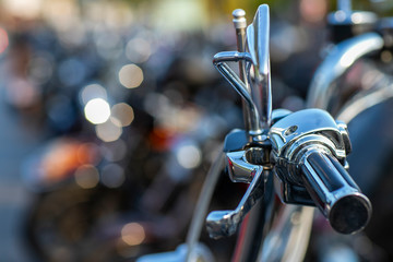 The chromed handlebar of a motorcycle.  View of motorcycle handlebar in the background many motorbikes blurred. 