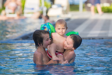 Obraz na płótnie Canvas Adorable happy little child, toddler boy, having fun relaxing and playing with his older brothers in a pool on sunny day during summer vacation