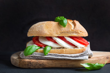 Caprese sandwich: Mozzarella, tomatoes, basil, italian bread, olive oil. Black background.