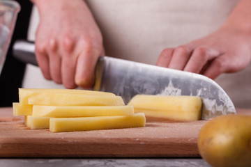young woman in an apron cuts potatoes
