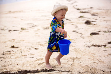 Cute toddler baby boy playing with beach toys on tropical beach