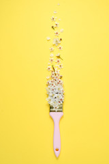Creative flower arrangement. Paintbrush With Blossoms on pastel yellow background. Minimal nature flat lay. Top view, copy space