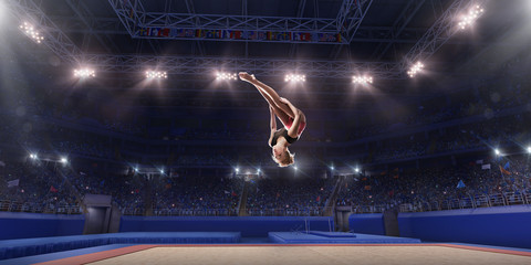 Female athlete doing a complicated exciting jump trick in a professional gym. Girl perform stunt in bright sports clothes