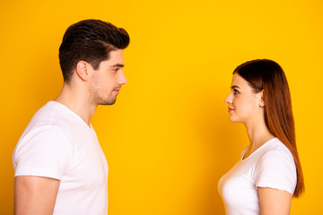 Close up side profile photo funny beautiful she her he him his guy lady stand opposite wait first who take eyes off each other lovely look wear casual white t-shirts outfit isolated yellow background
