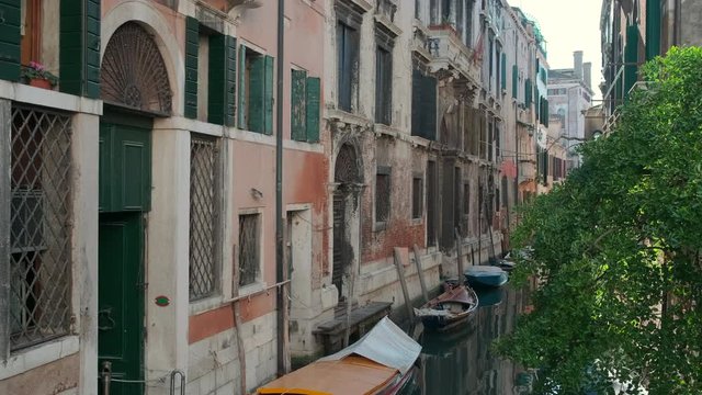Beautiful venetian street in daytime, boats are moored on small canal,