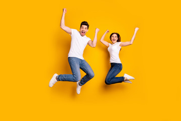 Fototapeta na wymiar Full length body size photo funky she her he him his pair jumping high raised fists yell scream shout loud cheerleader football fans wear casual jeans denim white t-shirts isolated yellow background