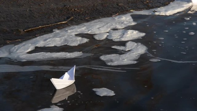 Toy paper boat on blue water at the edge of the shore covered with foam.