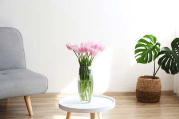 Empty apartment with minimal loft style interior, wooden floor and glass vase with bouquet of tulips on foreground and blank wall with a lot of copy space for text on background. Close up.