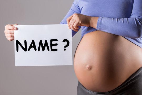Image of close up stomach of pregnant woman holding paper with question name on gray background.