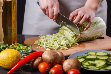 A young woman in a gray apron cuts chinese cabbage