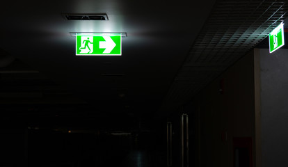 Green fire escape sign hang on the ceiling in the office at night.
