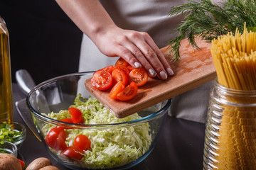 young woman in a gray apron adds cherry tomatoes to a salad
