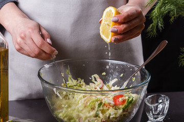 A young woman in a gray apron adds lemon juice to a cabbage salad