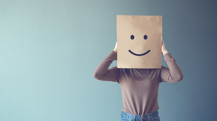 Woman covering his face with a smiling face emoticon, copy space. 