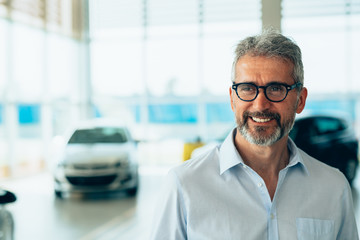 portrait of senior bearded man wearing eyeglasses in car showroom