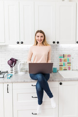 Young Woman in kitchen with laptop computer looking recipes, smiling. Food blogger concept