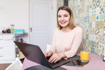 Smiling young woman using laptop in the kitchen at home