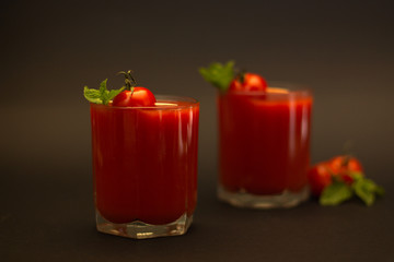 Two glasses of tomato juice with cherry tomatoes and mint with a black background