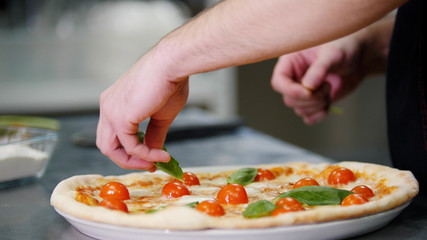 Obraz na płótnie Canvas Restaurant kitchen. A chef decorating the pizza with greenery