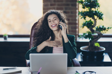 Portrait satisfied funny cute lady executive content enjoy break have dialogue friend colleague touch chest laughter sit chair desk fashionable jacket long wavy curly hairstyle cozy company