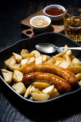 fried pork sausages with potatoes in frying pan for lunch, vertical