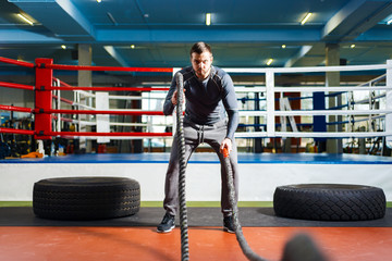 Obraz premium young guy trains strength fitness. man doing strength exercise with ropes.