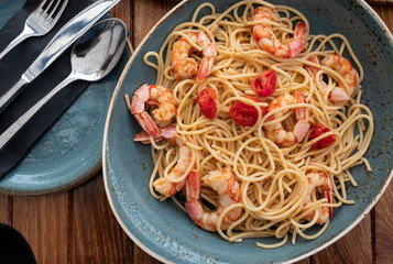 blue dish of spaghetti with prawns and pieces of tomatoes on wooden table